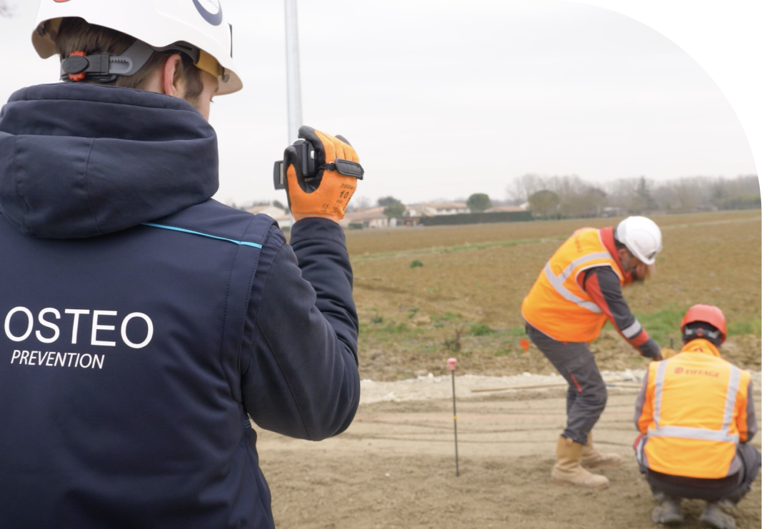 Un homme avec une veste My Ostéo Prévention film deux personnes entrain de travailler dans les champs 