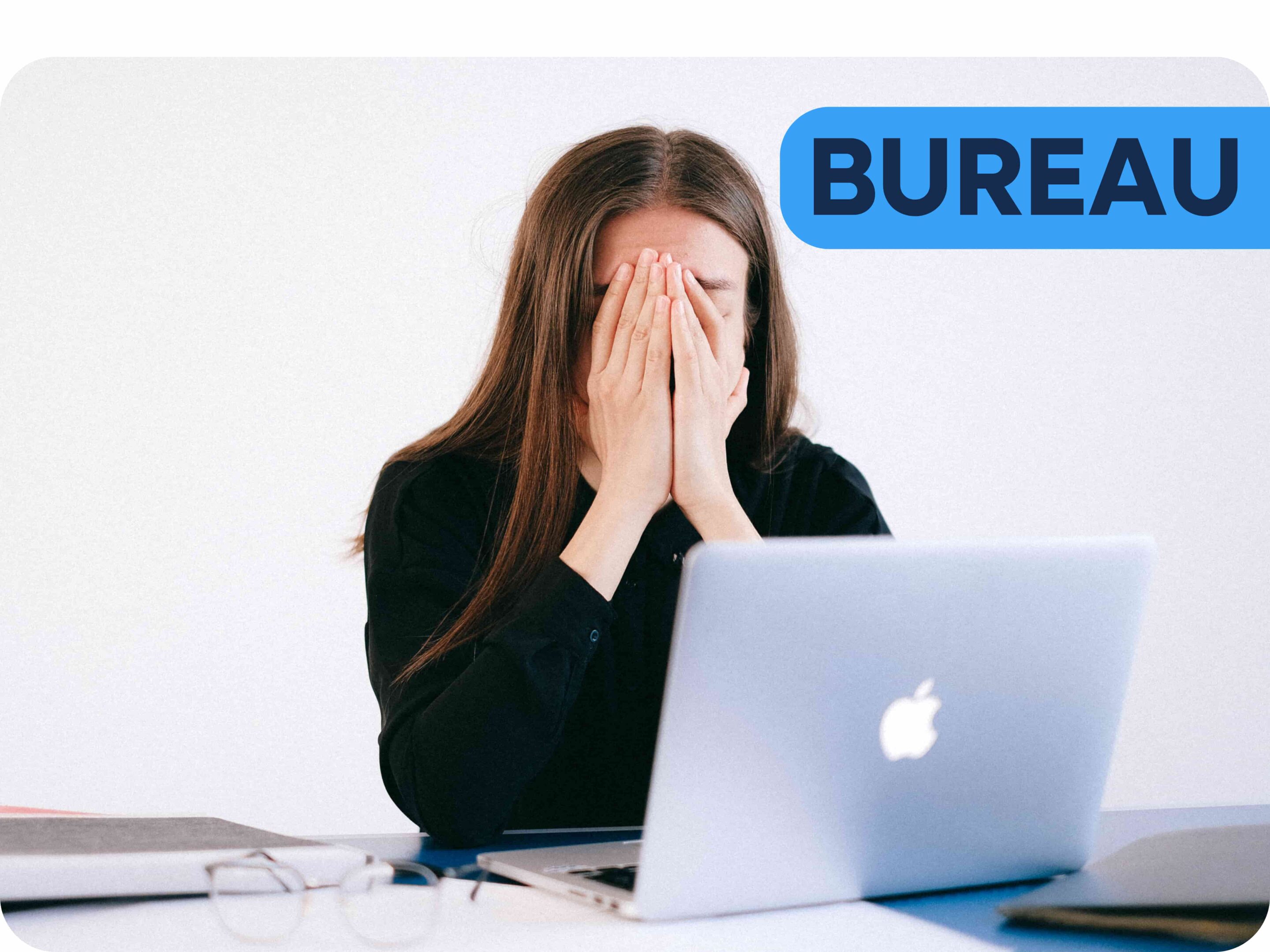 Femme brune aux cheveux longs assise à un bureau derrière son ordinateur avec sa tête dans les mains car elle est stressée par son travail