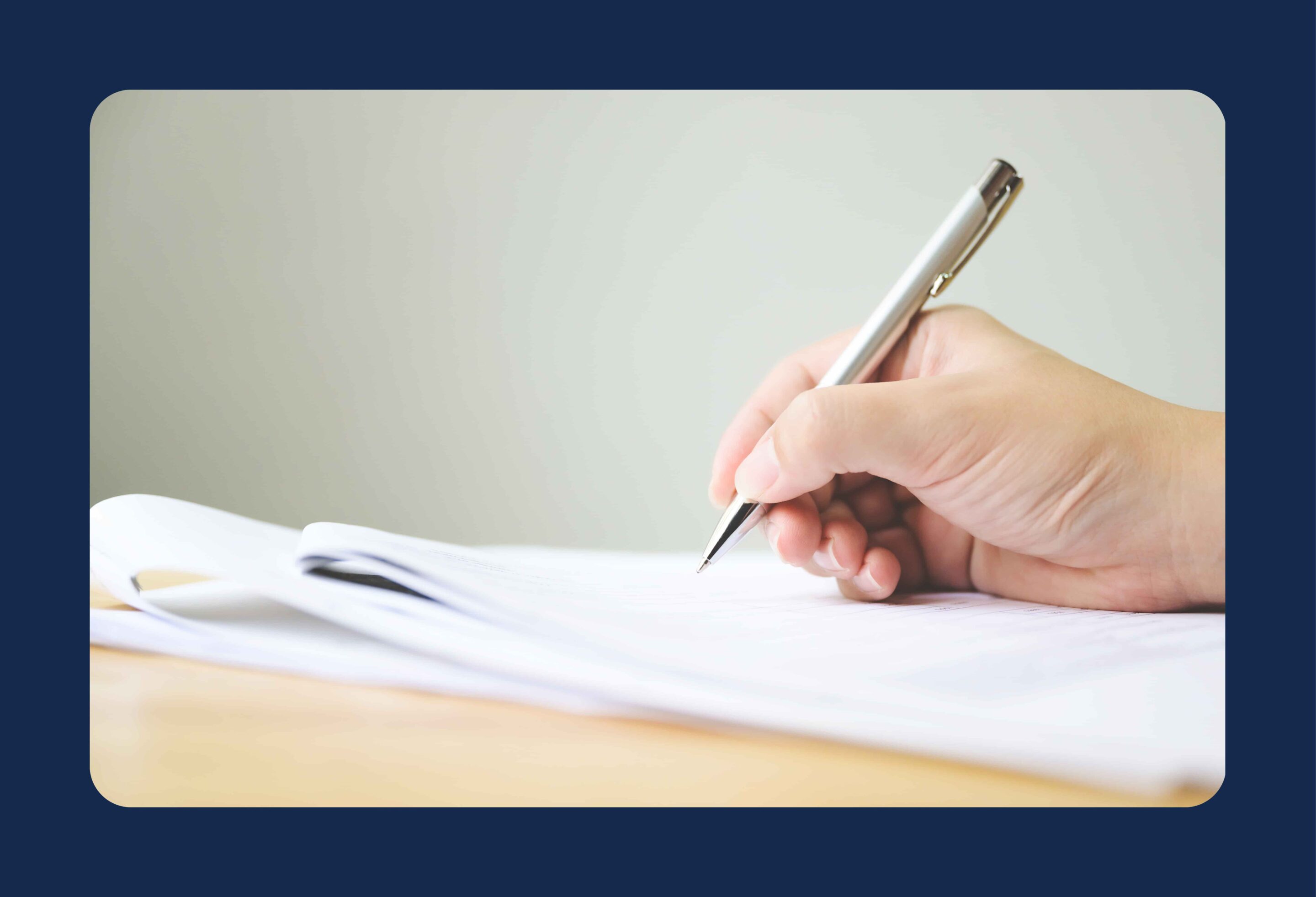 Main en train d'écrire avec un stylo sur une feuille qui est posée sur une table en bois