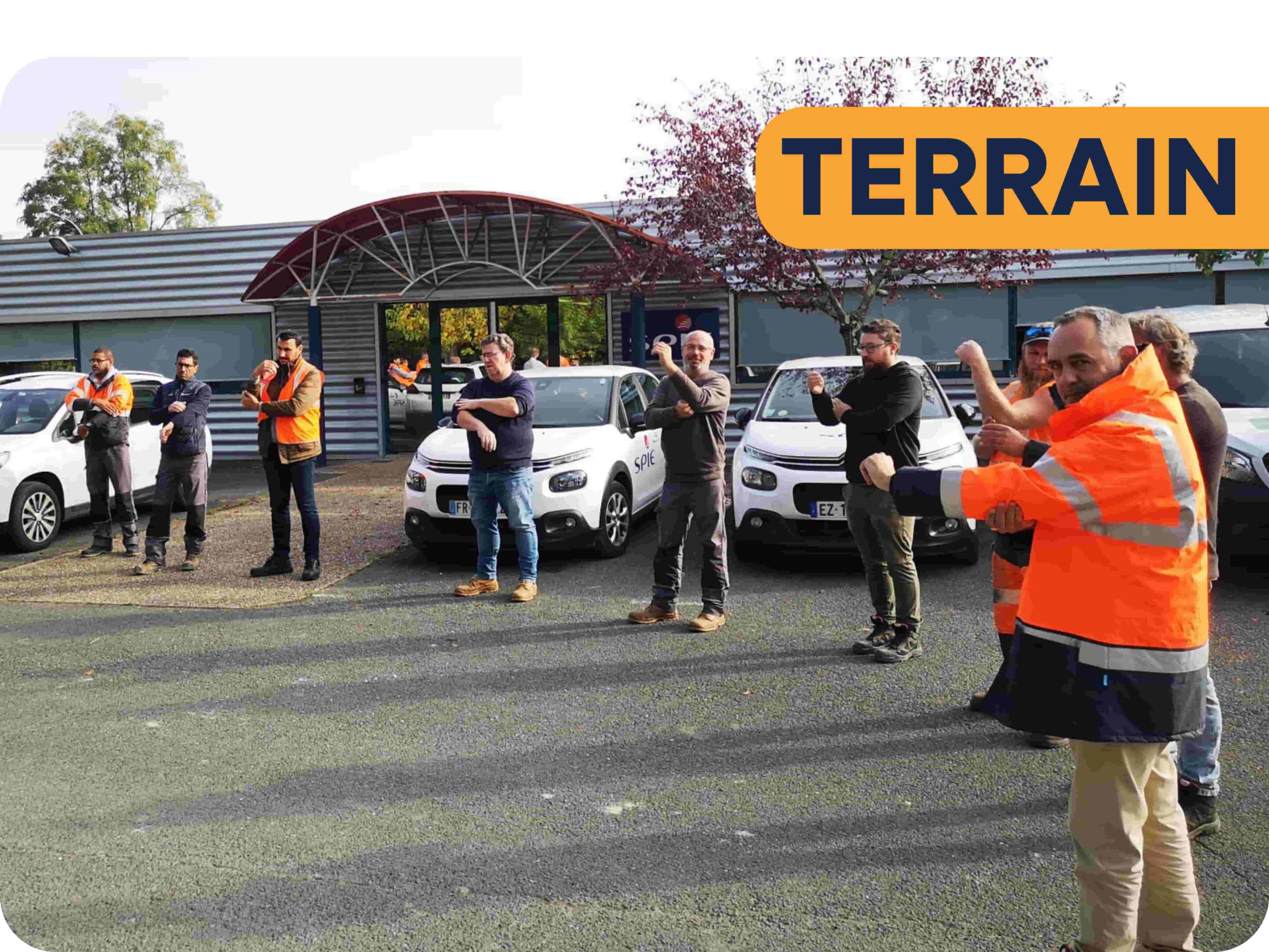 Groupe d'employés dans le secteur opérationnel qui pratiquent le réveil musculaire en cercle sur un parking devant des voitures